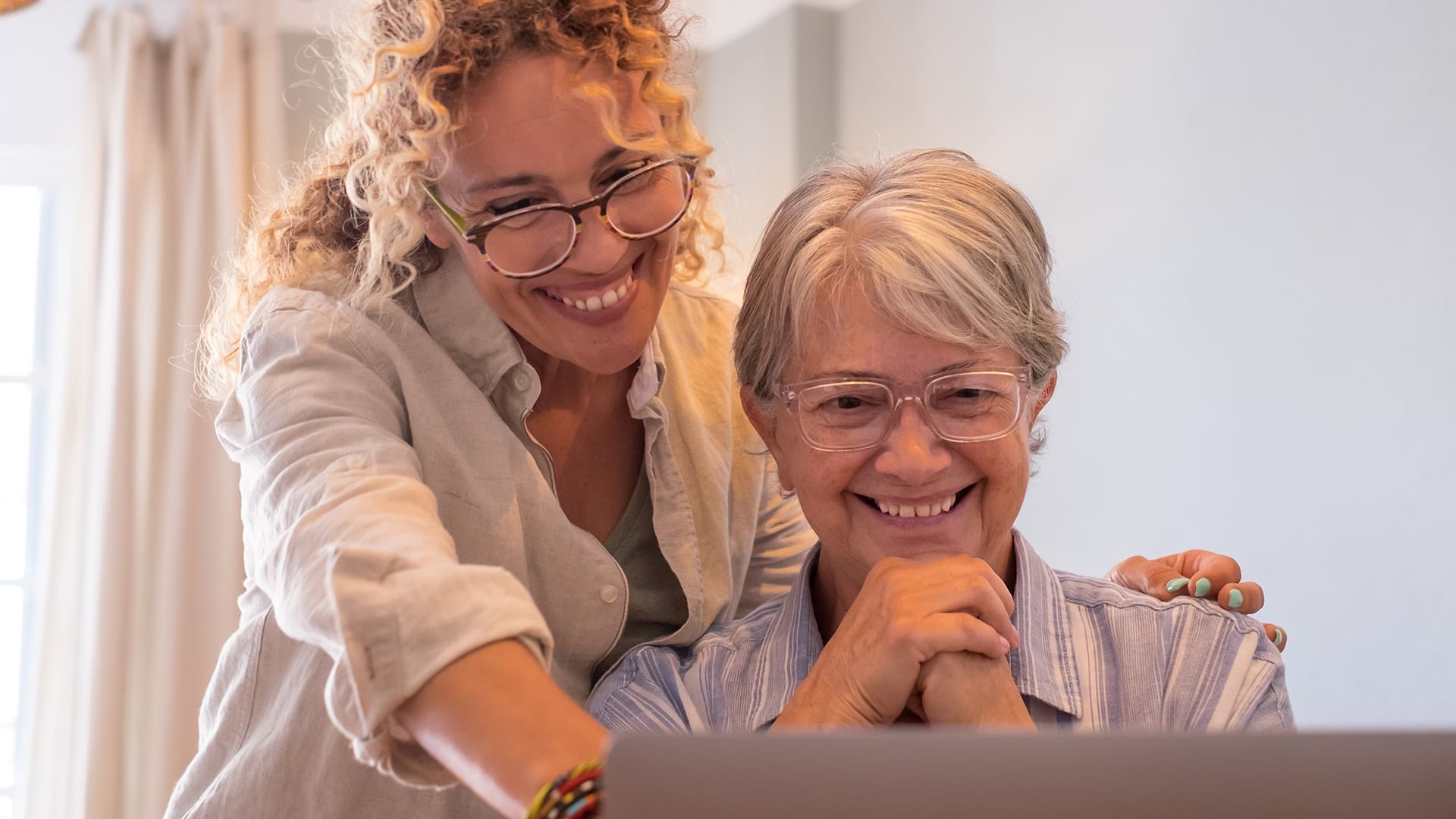 senior woman and her adult daughter smiling and pointing at their laptop screen