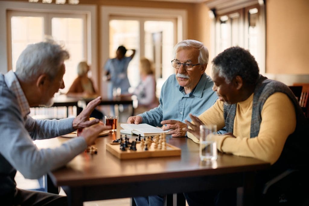 Senior man talking to his friends who are playing chess at retirement community